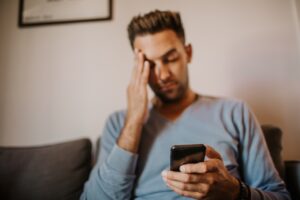 Man sitting on couch looking at phone with depressed porn addiction signs expression.